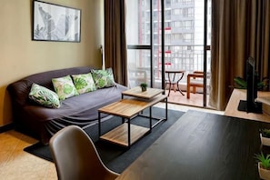 A modern living room with a sofa, a coffee table, a TV, and a balcony with a view of buildings.