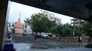 A street view with a pink temple, parked cars, and a blue trash bin labeled "ARISTO". - Hotel The Grand Om Krishna (Dwarka)