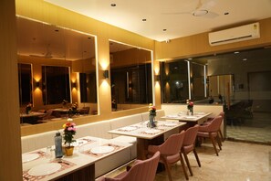 A restaurant with long tables, mirrored walls, and a modern interior. - Hotel The Grand Om Krishna (Dwarka)