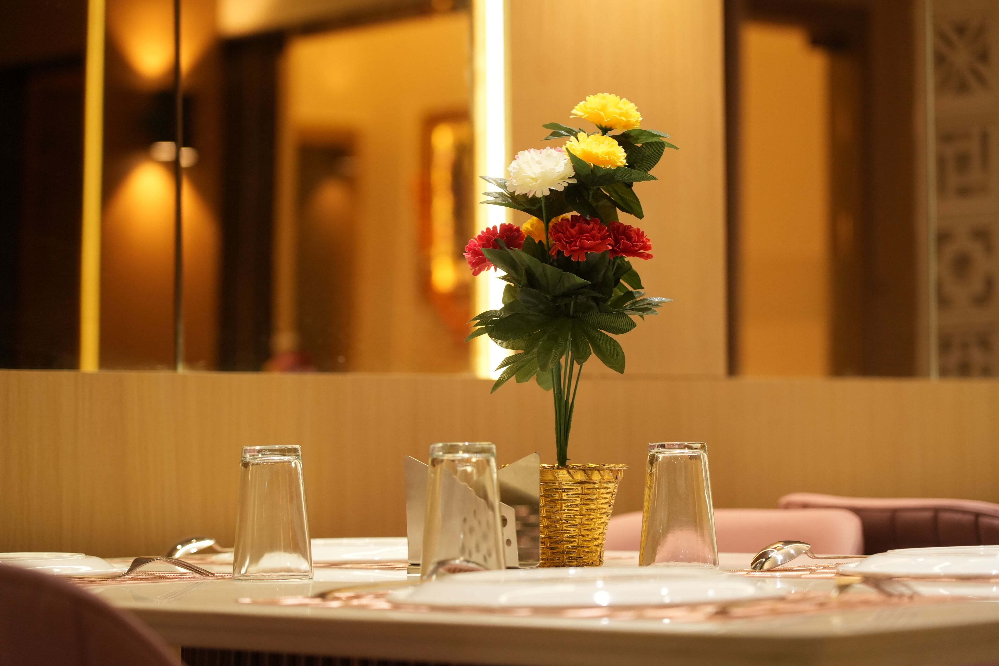 A dining table with a vase of flowers, a glass, and a spoon.