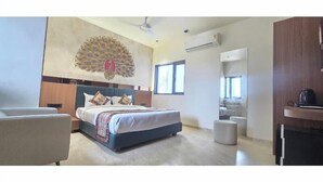 A modern hotel room with a large bed, a sitting area, a kitchenette, and a large window. - Hotel The Grand Om Krishna (Dwarka)