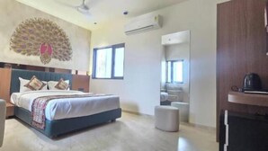A bedroom with a bed, a chair, a vanity, and a peacock-themed wall decoration. - Hotel The Grand Om Krishna (Dwarka)