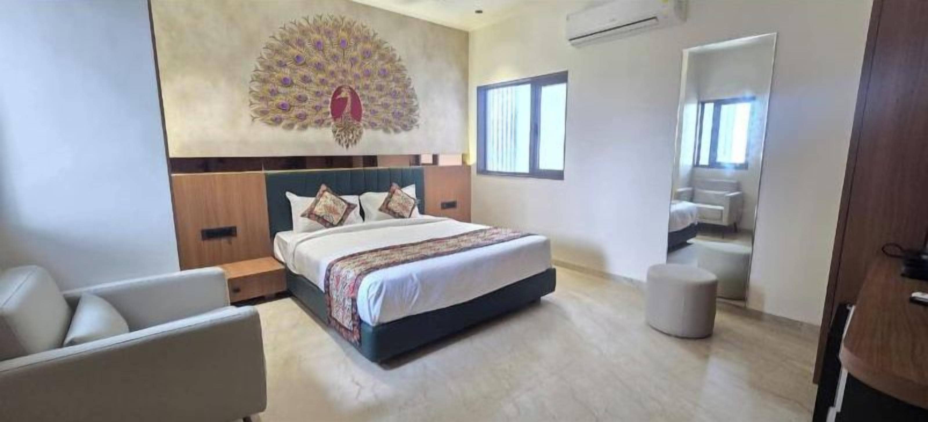 A modern hotel room with a large bed, a seating area with a chair, a decorative wall piece, and a large mirror.