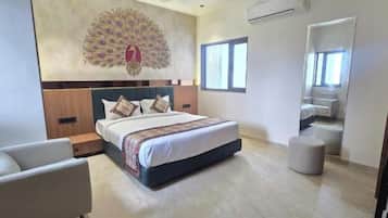 A modern hotel room with a large bed, a seating area with a chair, a decorative wall piece, and a large mirror.