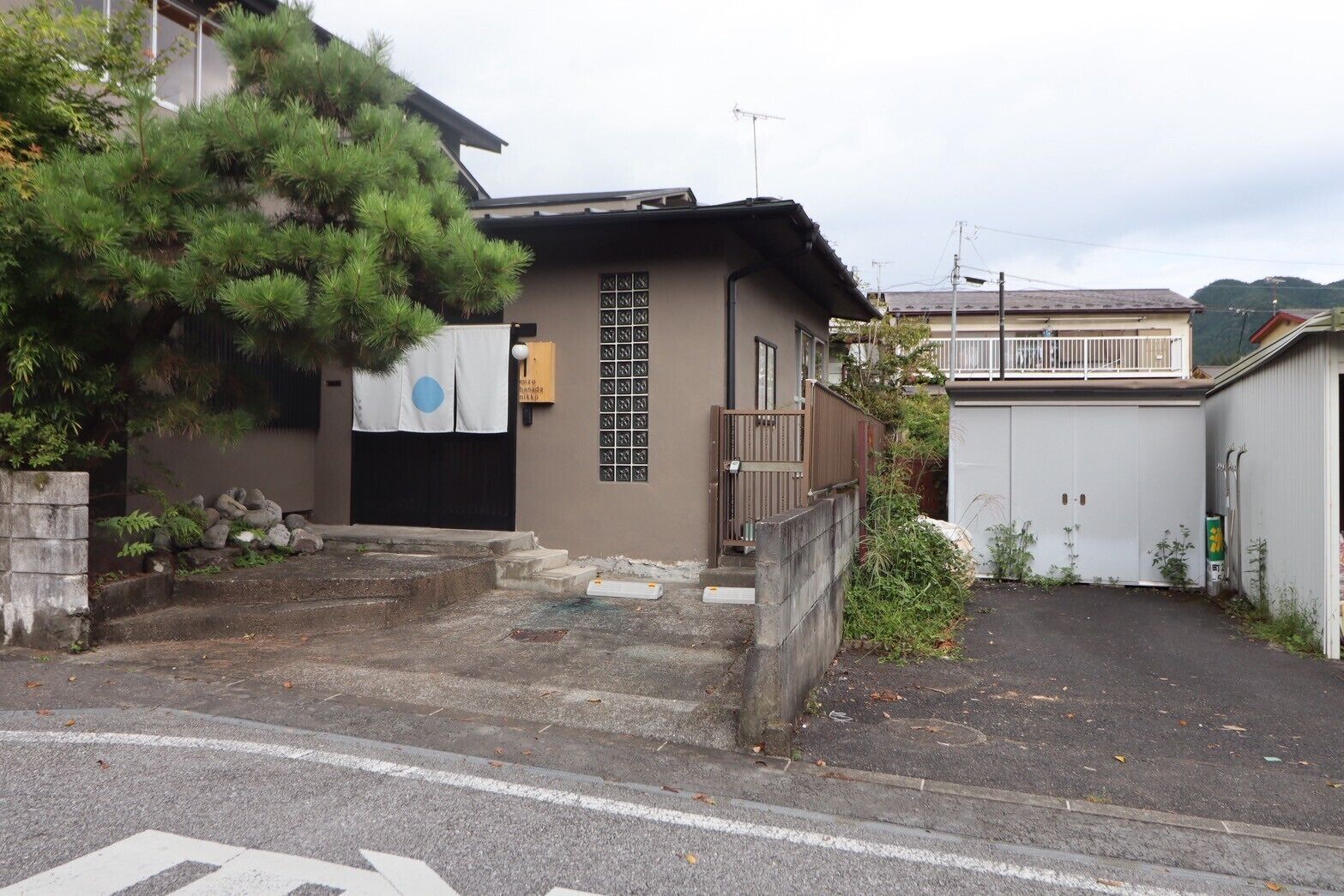 A residential building with a small front yard, a gate, and a driveway leading to a garage.