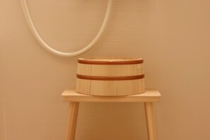 A wooden stool with a cylindrical object on top, possibly a container or a decorative piece, against a plain wall. - MizuhanadaNikko (Nikko)