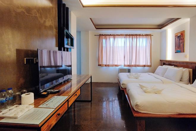 A hotel room with a TV, a desk with a computer, a bed, and a window with curtains.