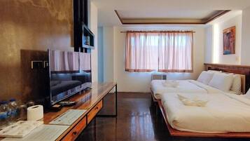 A hotel room with a TV, a desk with a computer, a bed, and a window with curtains.