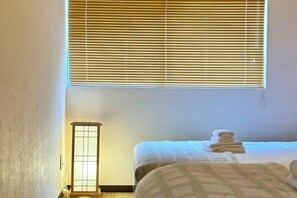 A hotel room with a bed, a bedside table, a lamp, and a window with blinds. - Kitagatsukyo｜Direct train to Osaka Castle, Shinsaibashi, and Tsutenkaku (Osaka)