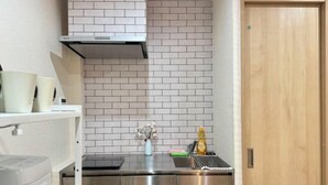 A compact kitchen with a stainless steel range hood, a white tiled backsplash, and a wooden door. - Kitagatsukyo｜Direct train to Osaka Castle, Shinsaibashi, and Tsutenkaku (Osaka)