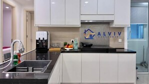 A modern kitchen with white cabinets, a black countertop, a built-in stove, and a water dispenser.