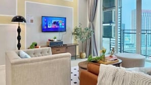 A modern living room with a flat-screen TV, a sofa, a coffee table, and a view of the city through large windows.