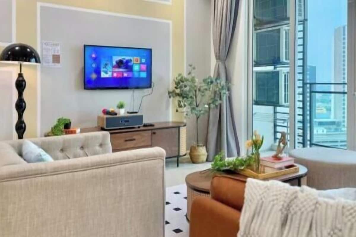 A modern living room with a flat-screen TV, a sofa, a coffee table, and a view of the city through large windows.