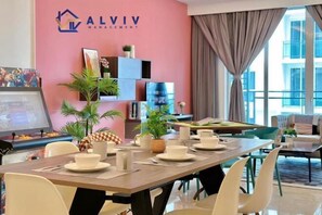 Moderni hotellihuone, jossa on vaaleanpunainen tehosteseinä, ruokailutila biljardipöydällä sekä näkymä kaupunkimaisemaan.