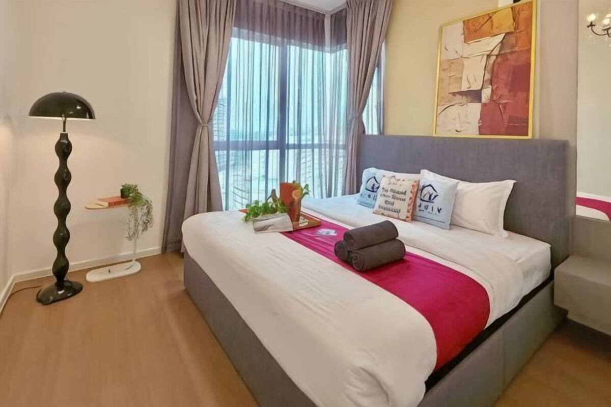 A neatly made bed with a red throw, a bedside lamp, and a window with curtains.