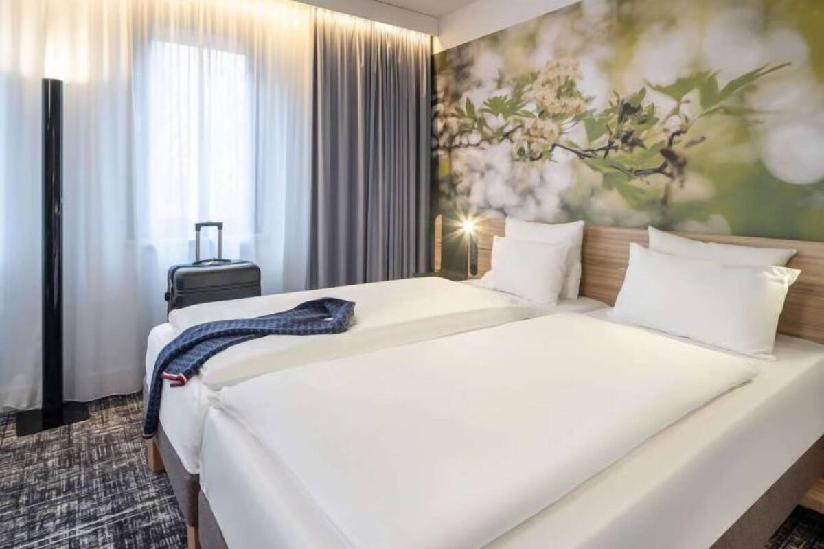 Habitació d'hotel amb un llit, una maleta, una taula de nit i una paret amb un mural floral.