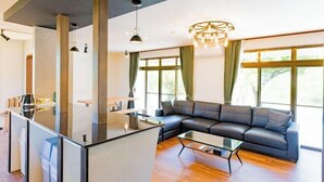 Una sala moderna con un comedor de cristal, un sofá de cuero negro y amplias ventanas con cortinas.