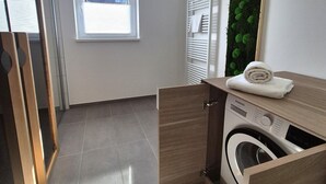A compact laundry room with a built-in washer and dryer, a wooden counter, and a window with blinds. - Winterberg comfort for 4 guests (Winterberg)