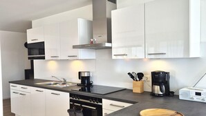 A modern kitchen with white cabinets, a black countertop, a stove, a coffee maker, and a wooden cutting board. - Winterberg comfort for 4 guests (Winterberg)