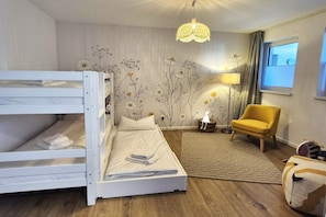 A bunk bed with a white headboard, a yellow armchair, a lamp, and a window with curtains.