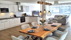 A modern kitchen with white cabinets, a wooden dining table set for six, and a city view through large windows. - Winterberg comfort for 4 guests (Winterberg)