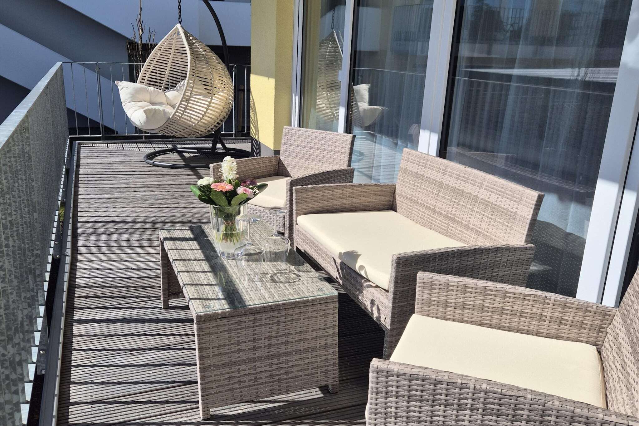 A balcony with wicker furniture, including a sofa and chairs, and a hanging chair.