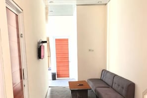 Un couloir avec un canapé, une table et une porte qui donne sur une pièce orange.