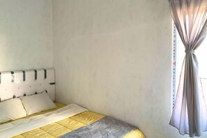 Un dormitorio con una cama, cabecera y ventana con cortinas.