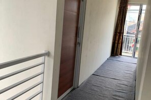 Un couloir étroit, avec une rambarde métallique d’un côté et une porte coulissante de l’autre.