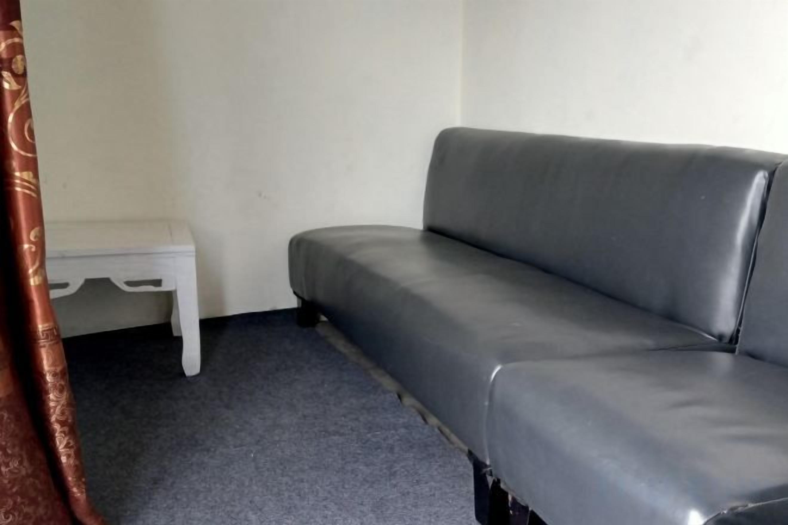 A grey sofa with a white side table in a room with a plain white wall and a grey carpet.