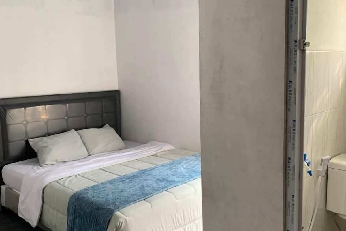 A bedroom with a bed, a headboard, a window, and a shower area.