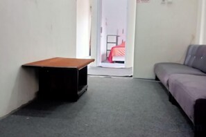 Une pièce comprenant une petite table, un canapé et une porte-fenêtre donnant sur une autre pièce où se trouve un lit.