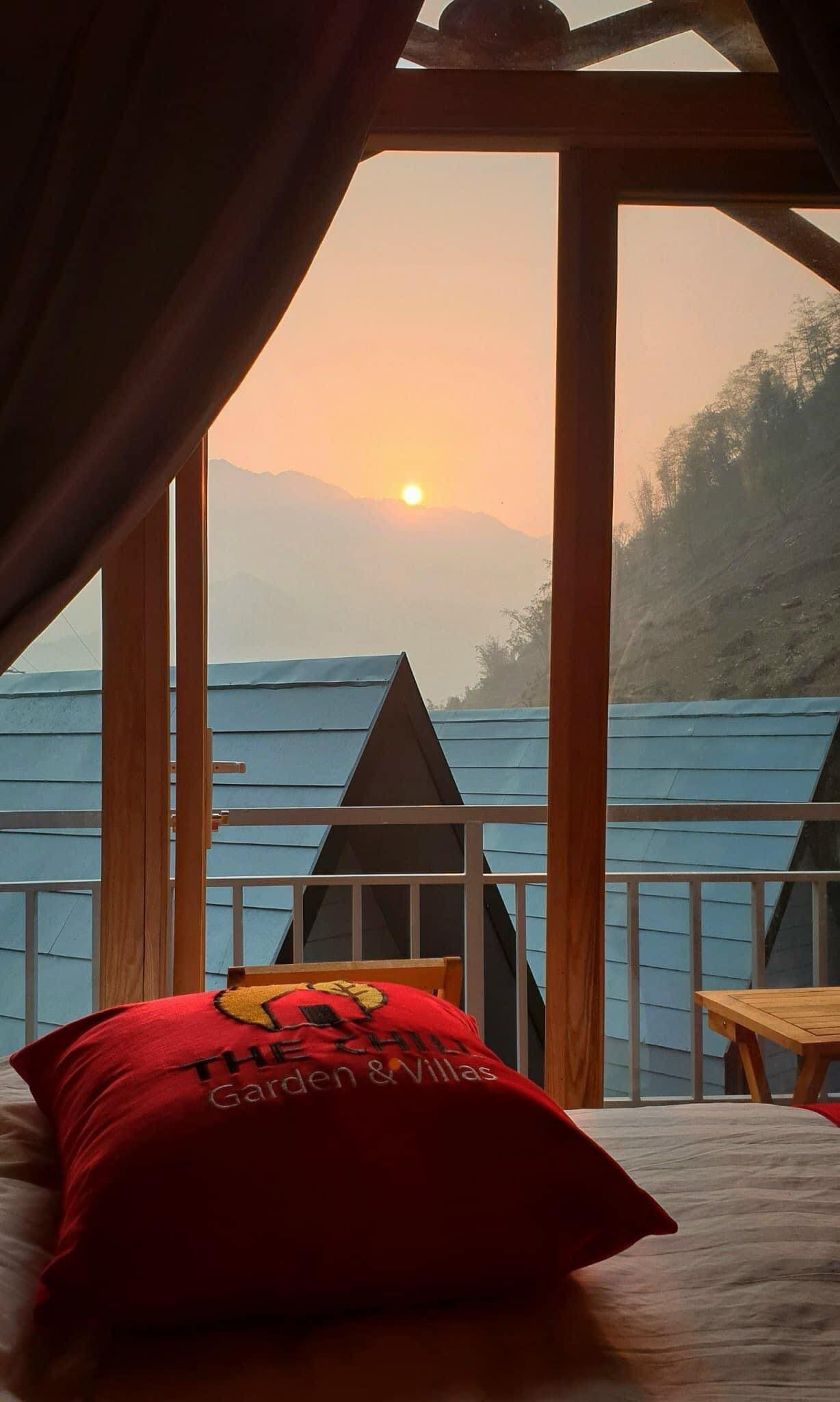 Een kamer met een bed, een rood kussen en uitzicht op de ondergaande zon boven het water.