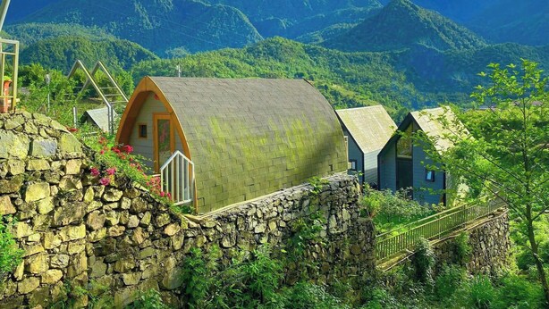 A traditional stone-walled building with a curved roof, surrounded by lush greenery and mountains in the background. - The Chill Garden Sapa (Ta Van)