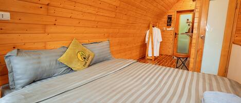 Una accogliente camera in legno con un letto, cuscini e un piccolo bagno.