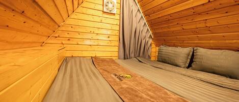 Une chambre confortable située dans les combles, avec des murs en bois, un lit recouvert d’une literie grise et un ventilateur au plafond.