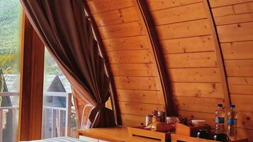 A cozy attic bedroom with a sloped ceiling, a bed with a blue blanket, a wooden bench with toiletries, and a view of the outside.