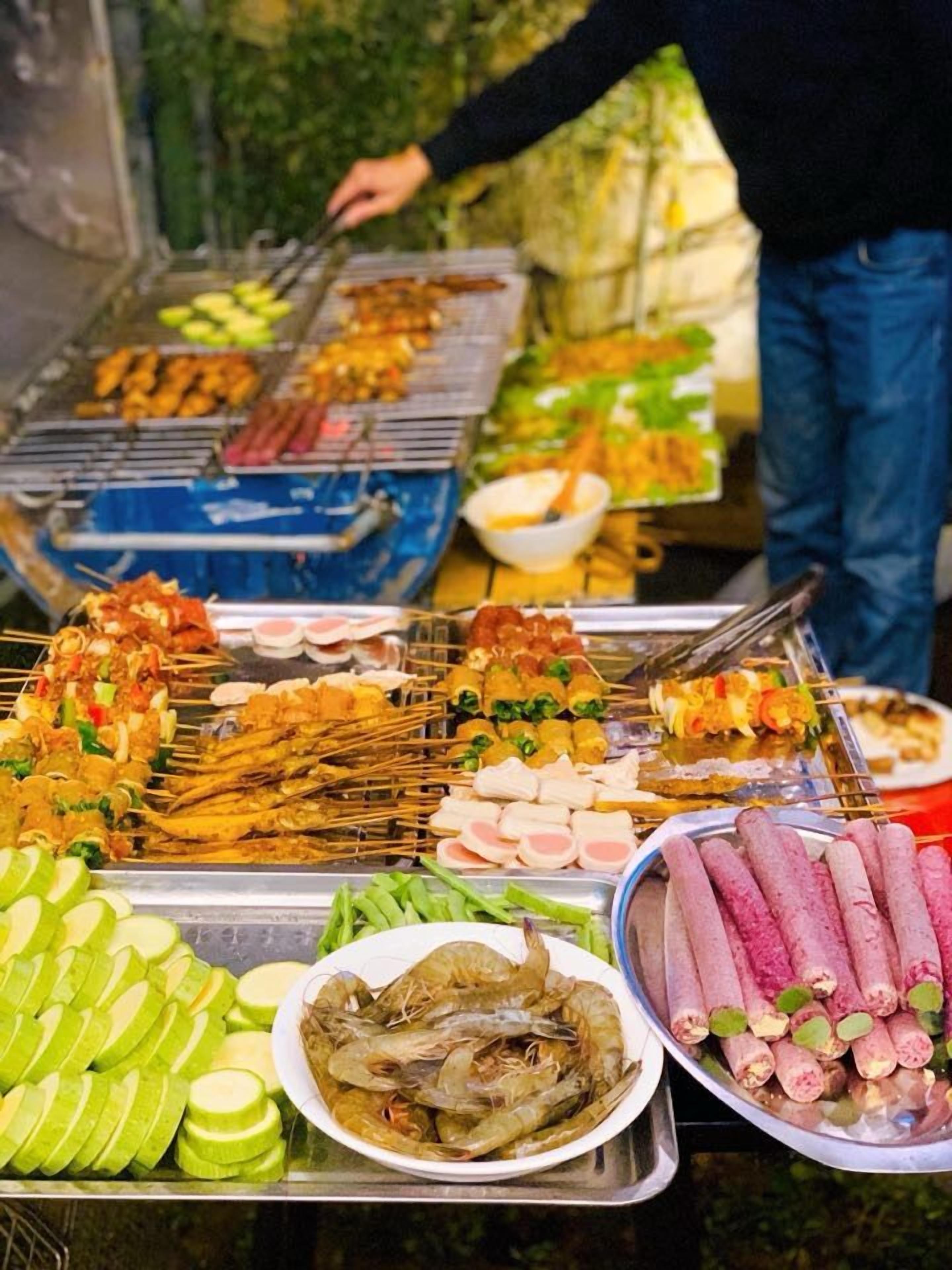 A variety of grilled foods including skewers, sausages, and shrimp, displayed on a table outdoors.
