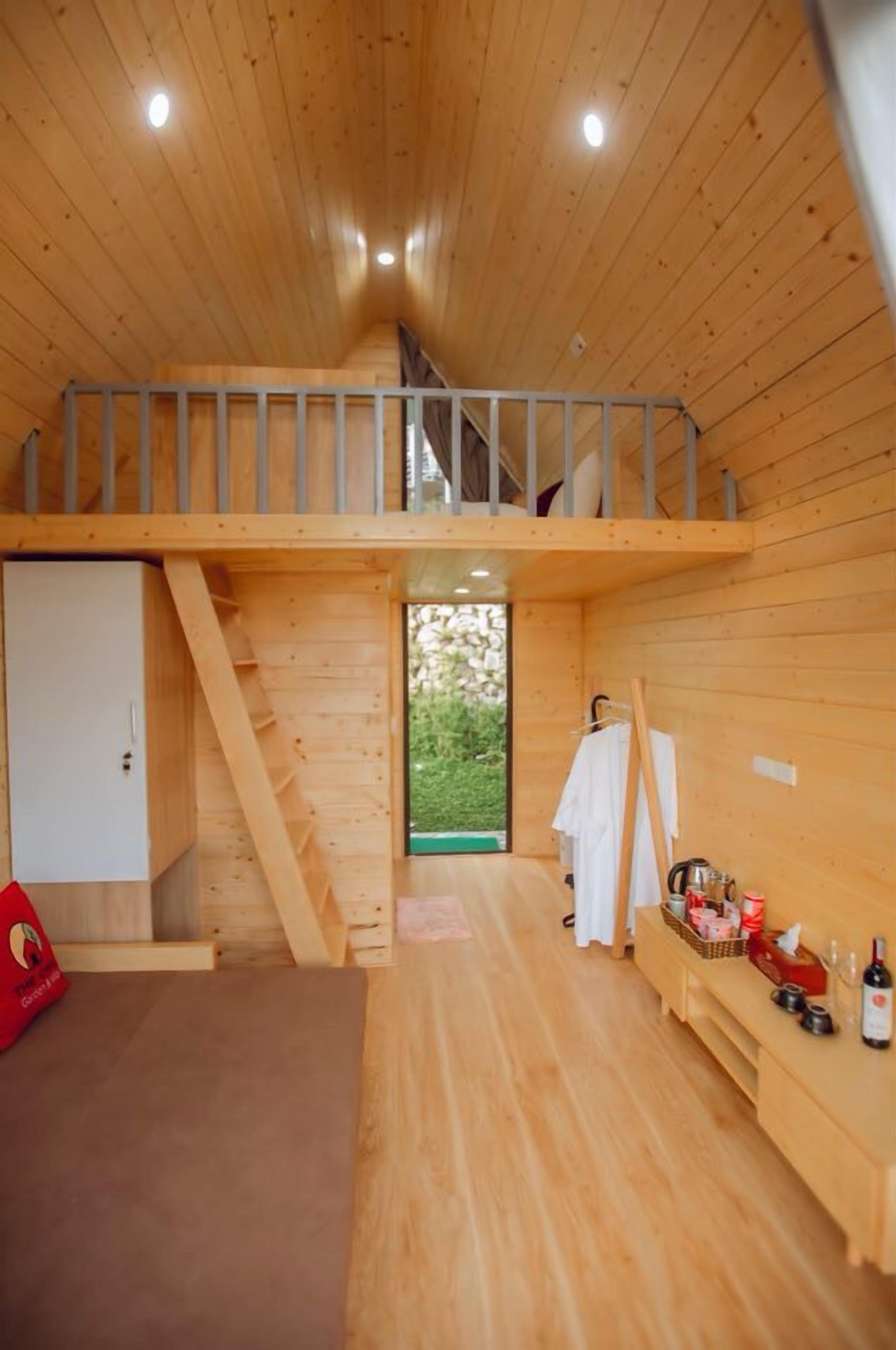 Interior de una cabaña de madera con habitación en el altillo, escalera, comedor y una pequeña cocina.