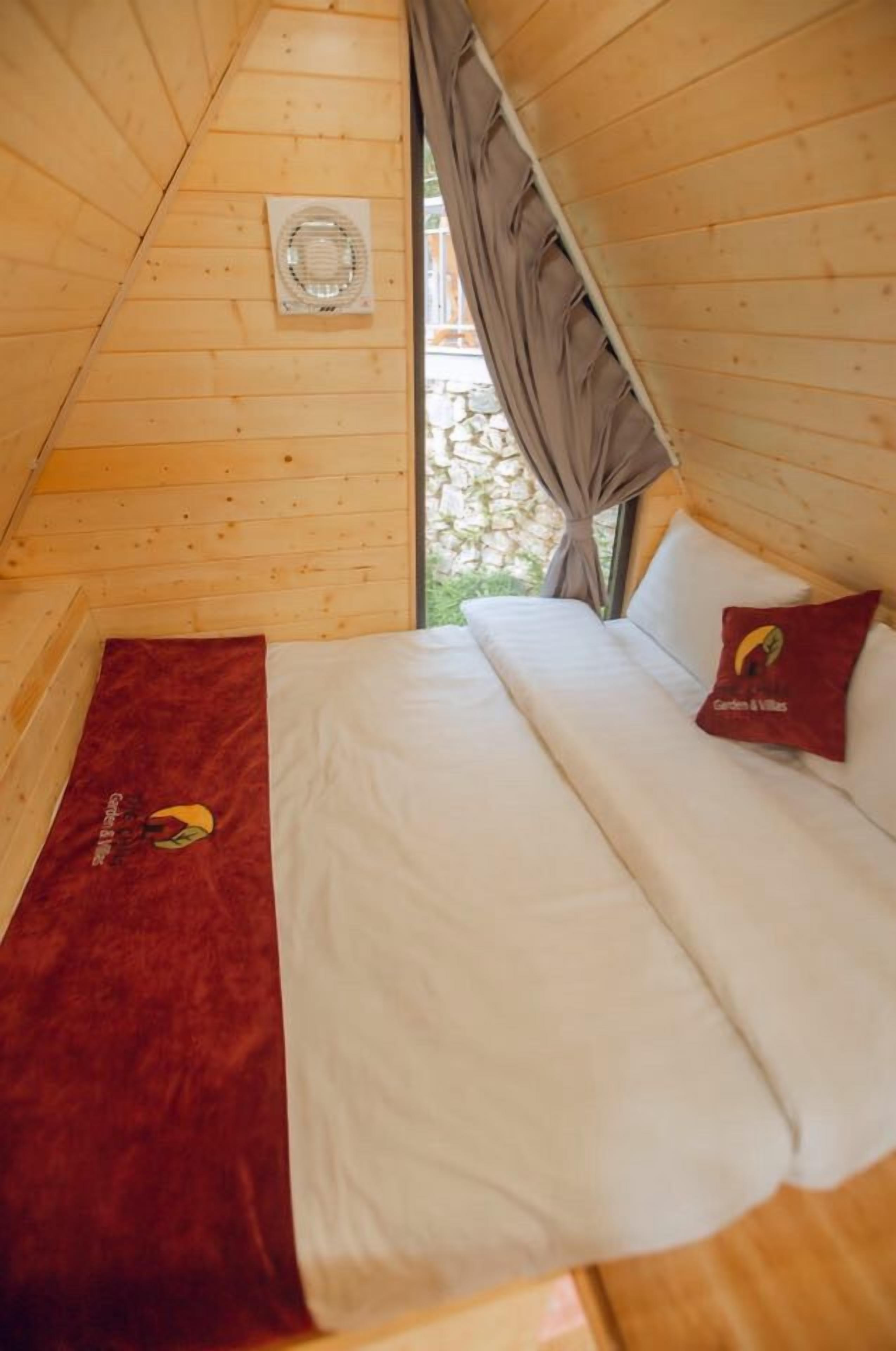 Una camera accogliente in legno con un letto, una finestra con tende e una piccola ventola a parete.