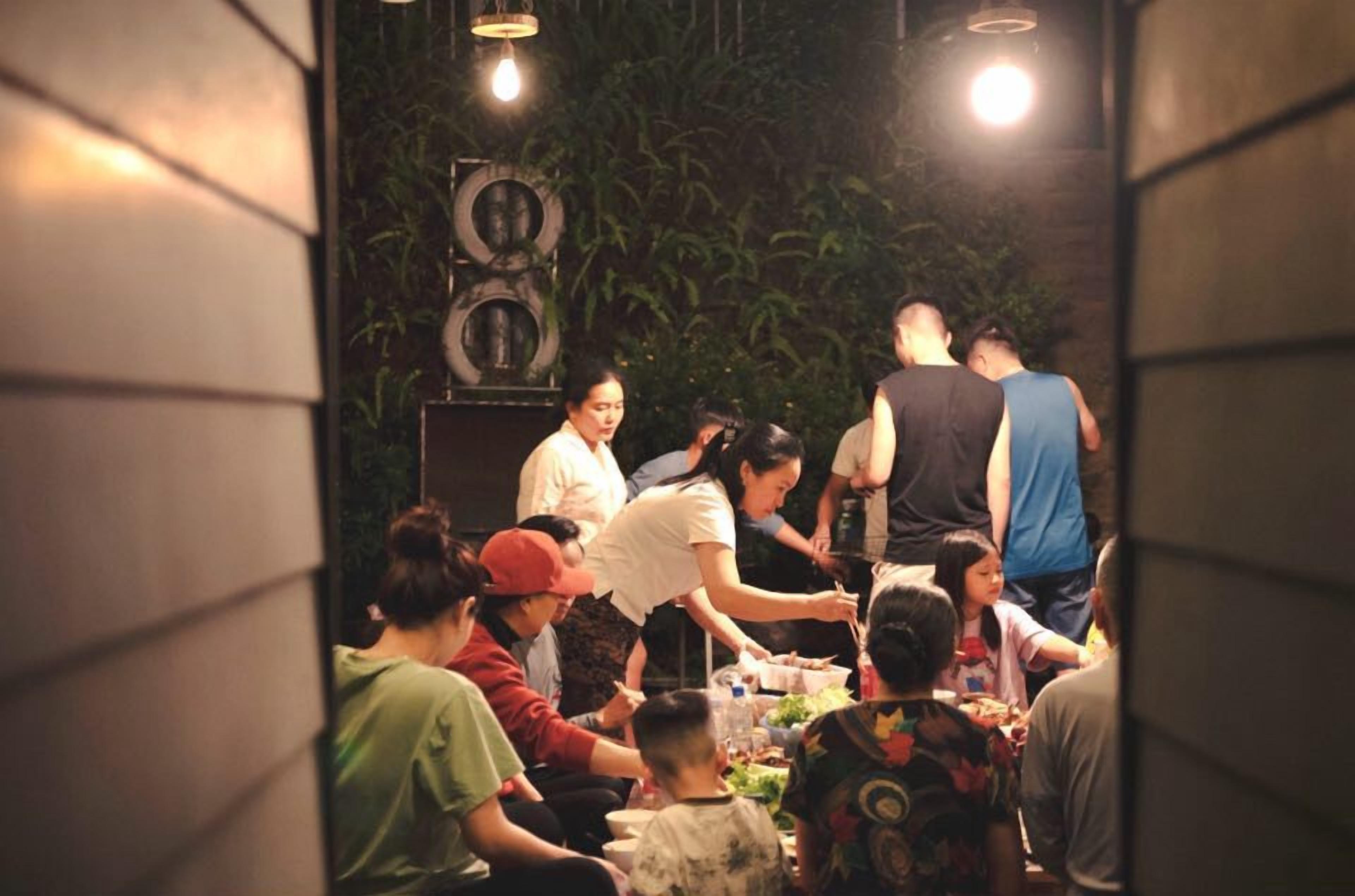 A group of people dining in a dimly lit room with a green plant wall and a speaker in the background.