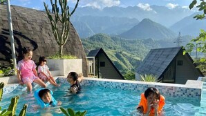 A swimming pool with a view of mountains, surrounded by small houses and greenery. - The Chill Garden Sapa (Ta Van)