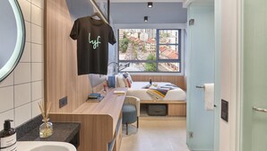 A compact hotel room with a bed, a small desk, a mirror, and a window with a city view. - lyf Farrer Park Singapore (Singapore)