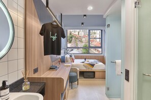A compact hotel room with a bed, a small desk, a mirror, and a window with a city view. - lyf Farrer Park Singapore (Singapore)