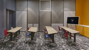 Un salón de conferencias con mesas, sillas, una pizarra y suelo alfombrado.