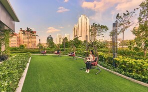 A rooftop garden with artificial grass, swing chairs, and a person sitting. - lyf Farrer Park Singapore (Singapore)