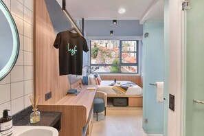 A modern bathroom with a wooden vanity, a hanging towel, and a bed with a view of buildings. - lyf Farrer Park Singapore (Singapore)