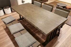 A long wooden table with six chairs, a small round table, and a trash bin.