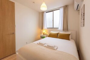 Ein Hotelzimmer mit Bett, Nachttischlampe, einem Fenster mit Vorhängen und einer Wandklimaanlage.