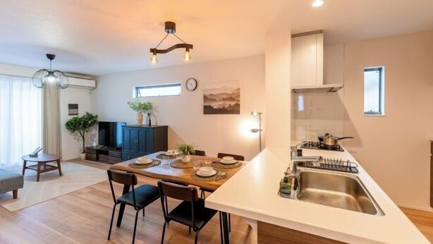 A modern kitchen with a central island, a dining area with a wooden table and chairs, and a living space with a sofa and a plant. - New open ! TabiTaimu・Momodani MOMO｜Near Tennoji Park & Shinsekai｜Direct Train to Osaka Castle (Osaka)